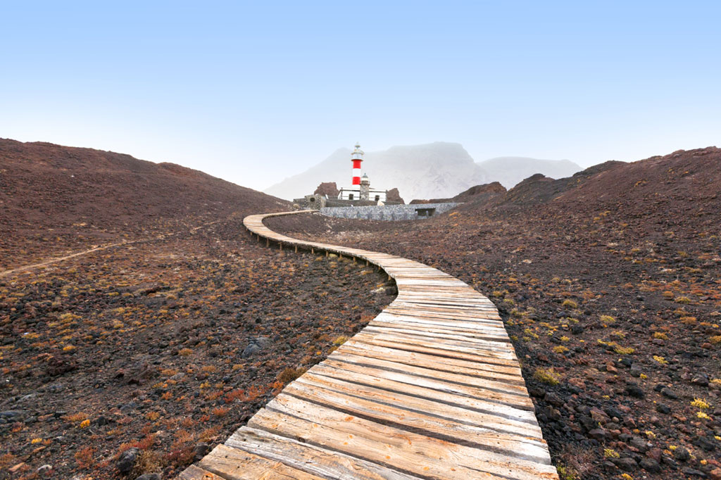 Passerelle en bois menant au phare de Punta de Teno, à Tenerife, avec des montagnes en arrière-plan.