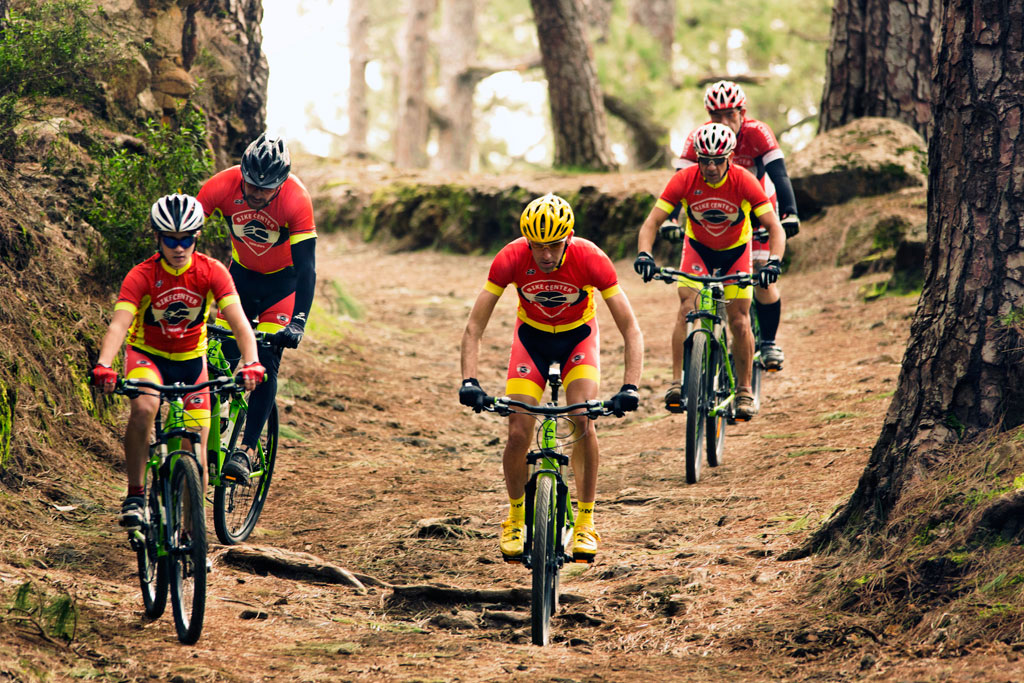 Des cyclistes sur un sentier forestier à Tenerife portant des uniformes rouges et noirs.