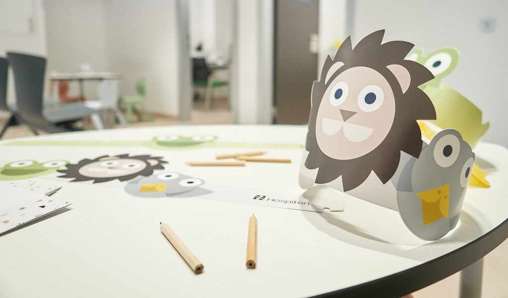 Table avec des matériaux d’artisanat pour enfants dans un hôpital de Tenerife, y compris des couronnes en papier avec des motifs d’animaux.