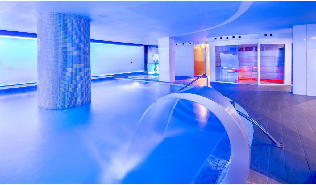 Piscine intérieure éclairée dans un hôtel à Tenerife avec jet d’eau et décoration moderne.