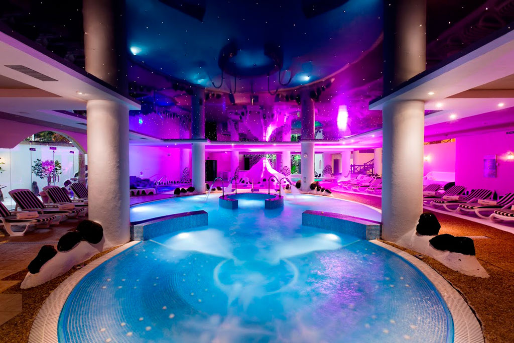 Piscine intérieure éclairée dans le spa de Tenerife avec des transats autour.