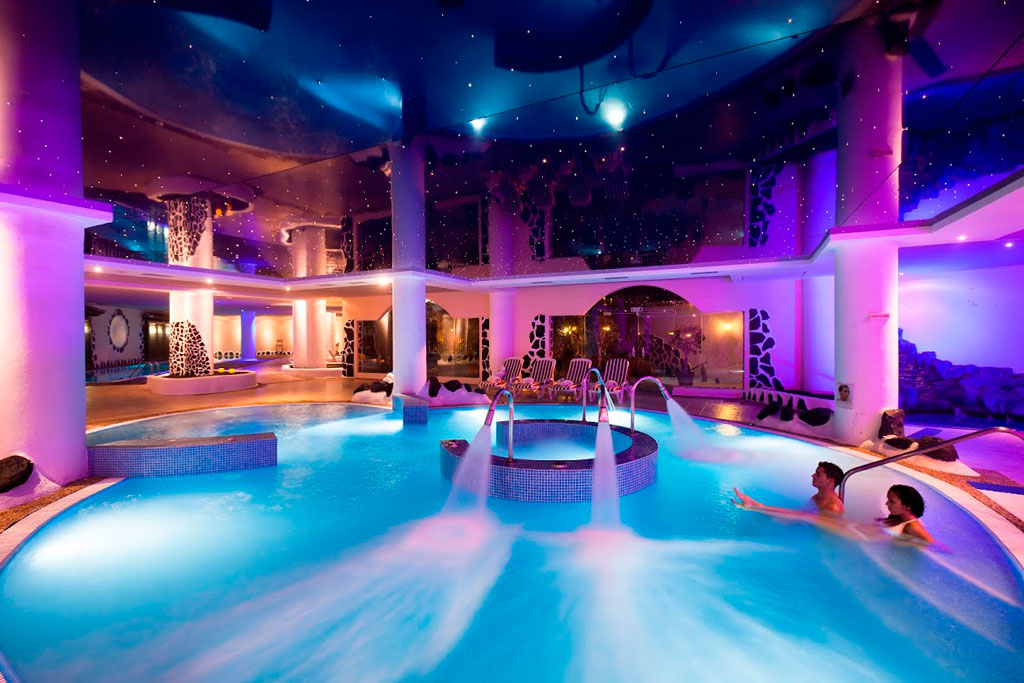 Piscine couverte éclairée dans un spa à Tenerife avec deux personnes qui se détendent.