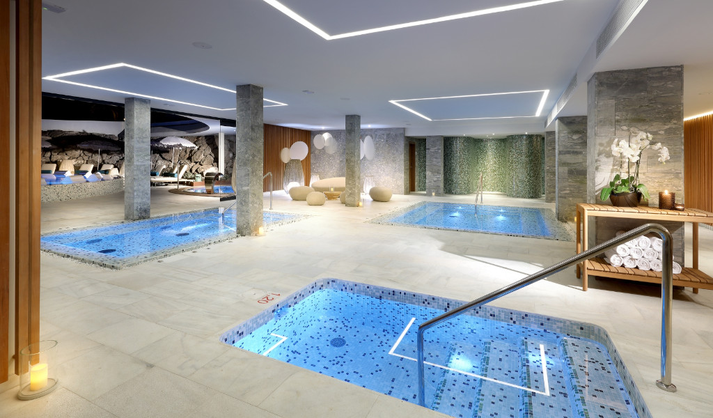 Piscine intérieure avec jacuzzi dans un spa à Tenerife, entourée de plantes et de lampes.