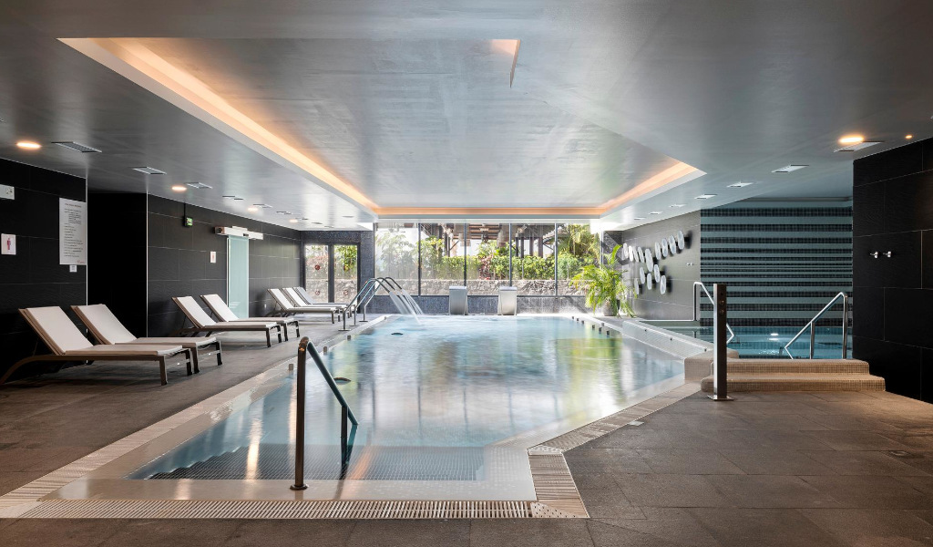 Piscine intérieure à Tenerife avec des transats et des plantes près des fenêtres.