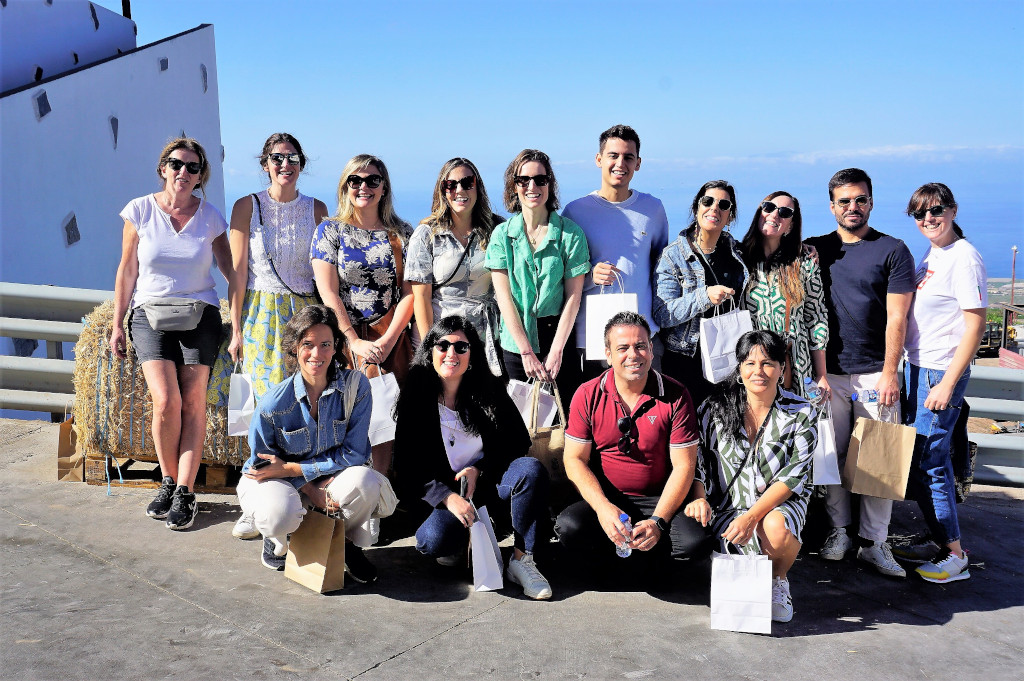 Groupe de personnes souriantes devant la mer, dans un endroit à Tenerife, avec des sacs cadeaux.