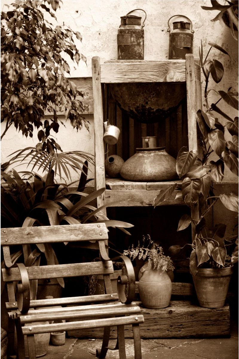 Banc en bois entouré de plantes et d’objets métalliques dans une cour rustique à Tenerife.