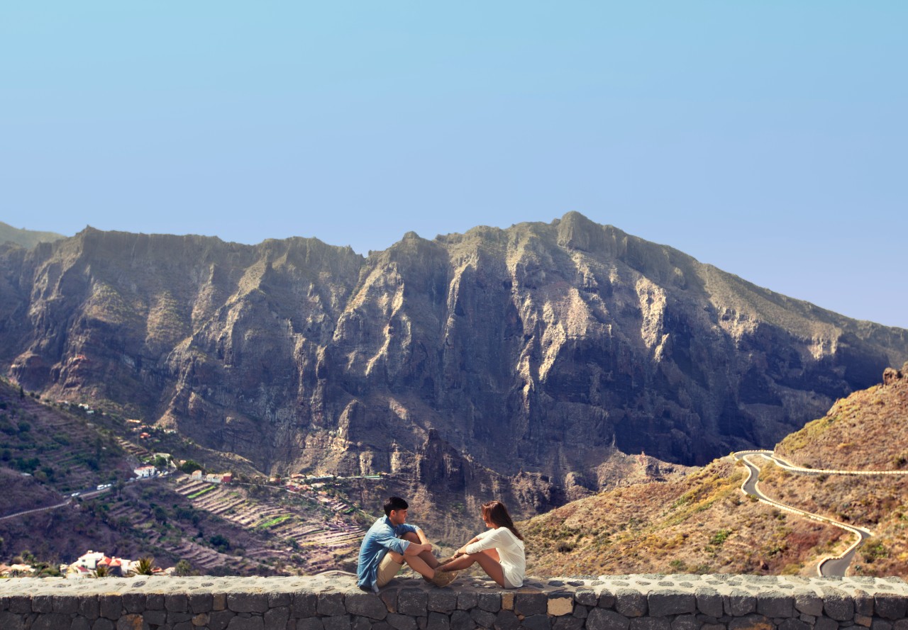Des gens assis devant les montagnes de Masca à Tenerife, avec un sentier sinueux en arrière-plan.