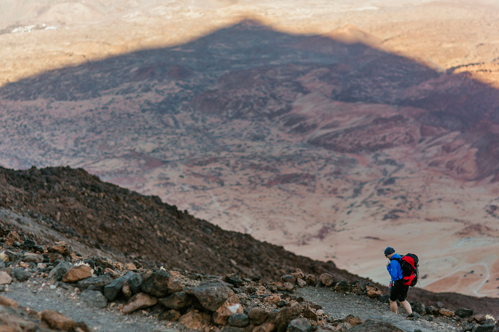 Personne marchant sur un sentier rocheux sur le mont Teide, à Tenerife, avec un paysage aride en arrière-plan.