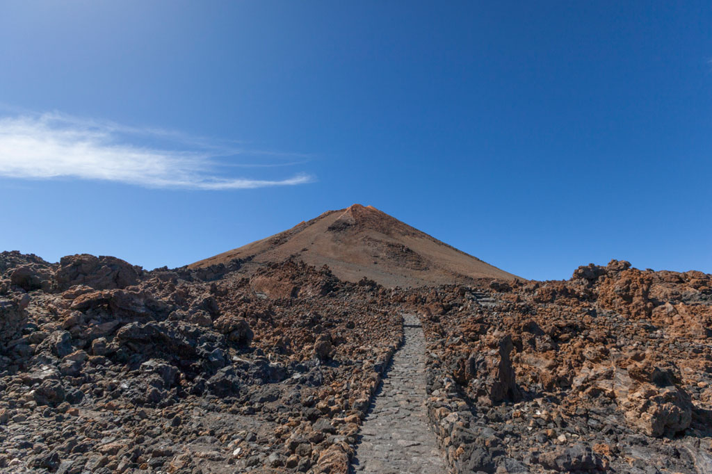 Un chemin de galets vers le mont Teide à Tenerife sous un ciel bleu.