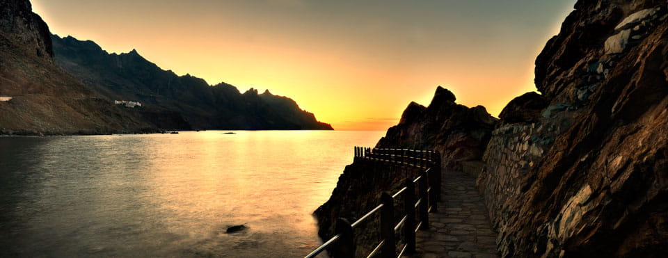 Sentier côtier au coucher du soleil à Tenerife avec vue sur la mer et les montagnes en arrière-plan.