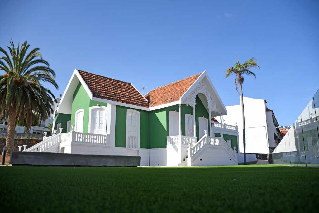 Vieille maison verte et blanche au toit rouge à Tenerife, entourée de palmiers et de pelouses.