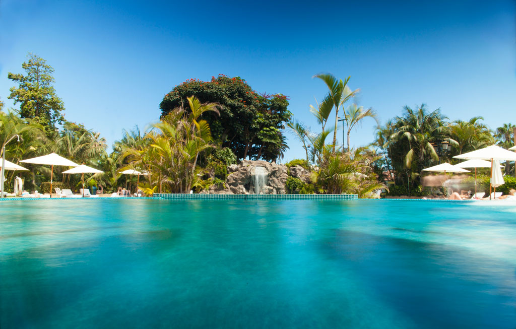 Piscine avec parasols et végétation tropicale dans un hôtel à Tenerife.